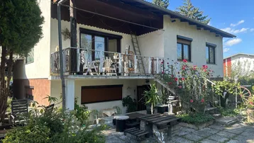 Hausfassade mit Balkon, Terrasse und einem kleinen Gartenbereich mit Sitzgelegenheiten.
