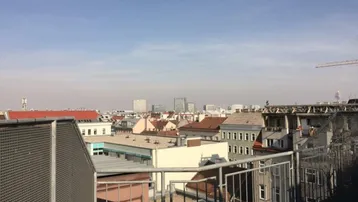 Panoramablick über die Dächer der Stadt mit urbaner Skyline im Hintergrund und Metallgeländer im Vordergrund.