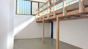 Heller, geräumiger Raum mit hohen Decken, großen Fenstern und einem robusten Holz-Zwischengeschoss.