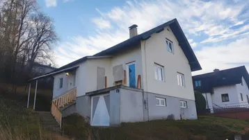 Haus auf einem Hanggrundstück mit Außentreppe und Satteldach unter blauem Himmel.