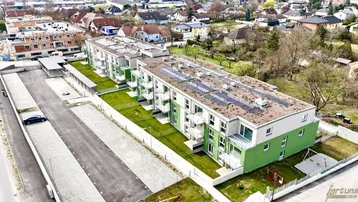 Luftaufnahme eines modernen Wohnkomplexes mit grünen Fassadenelementen, Balkonen und Photovoltaikanlage auf dem Dach.