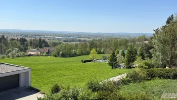 Weitläufige grüne Landschaft mit Fernblick, umgeben von Bäumen und einem klaren blauen Himmel.