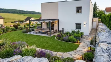 Modernes Haus mit gepflegtem Garten, großer Terrasse unter Pergola und weitem Blick ins Grüne.