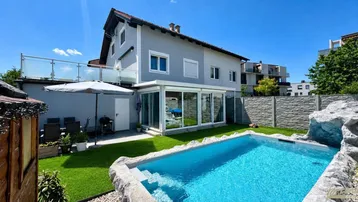 Modernes Haus mit Garten, privatem Pool und verglastem Wintergarten unter blauem Himmel.
