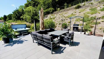 Geräumige Terrasse mit Lounge-Möbeln, Grillbereich und Whirlpool im Hintergrund.
