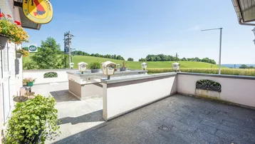 Gedeckte Terrasse mit Fliesenboden und weitem Blick über die grüne Landschaft.