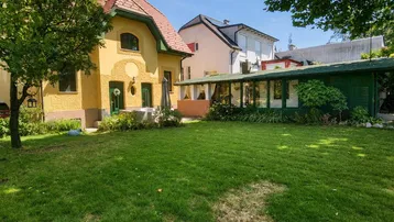 Sonnige Gartenanlage mit gepflegtem Rasen und einem charmanten gelben Haus im Hintergrund.