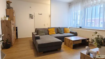 Helles Wohnzimmer mit gemütlichem Ecksofa, Holztisch und Laminatboden, ideal zum Entspannen.