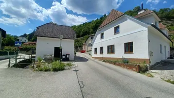 Wohnhaus in ländlicher Umgebung mit weißer Fassade, braunen Fenstern und Blick auf grüne Hügel.