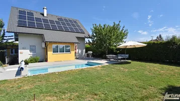 Hausfassade mit Solaranlage, großem Garten, Swimmingpool und gemütlicher Sitzecke im Freien.