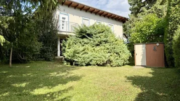 Außenansicht des Hauses mit gepflegtem Rasen, Bäumen und einem kleinen Gartenschuppen.
