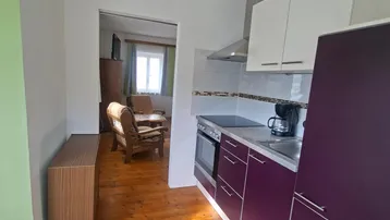 Kleine Einbauküche mit lila Fronten, Holzboden und Durchgang zum Wohn-/Schlafbereich.