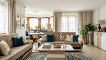 Helles Wohnzimmer mit beigen Sofas, Teppich und einem Essbereich im Hintergrund.