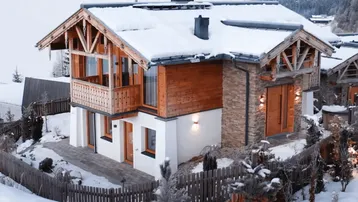 Charmantes Chalet im alpinen Stil, umgeben von verschneiten Bergen und einer idyllischen Winterlandschaft.