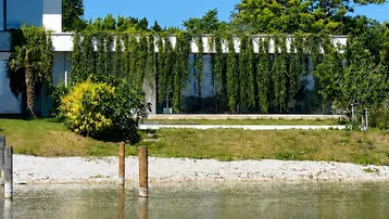 Moderne Architektur am Wasser mit begrünter Fassade und minimalistischem Design unter blauem Himmel.