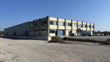 Großes Industriegebäude mit Büroflächen und Lagerhallen auf einem weitläufigen Gelände unter blauem Himmel.
