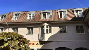 Gebäudefassade mit Mansarddach, Gaubenfenstern und einem Geschäft im Erdgeschoss.