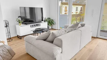 Helles Wohnzimmer mit modernem Sofa, TV-Möbel und Zugang zu einem Außenbereich.