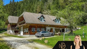 Traditionelles Holzhaus in ländlicher Umgebung mit viel Grün und einem geparkten Auto davor.