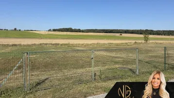 Ländliches Grundstück mit Zaun und weitem Blick über Felder unter blauem Himmel.