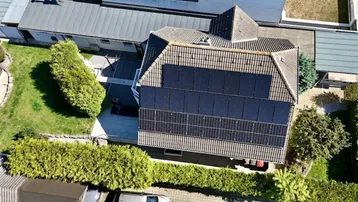 Dach des Einfamilienhauses mit installierter Photovoltaikanlage und grüner Umgebung.