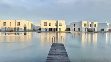 Malerischer Blick auf einen zugefrorenen See mit Steg und modernen Häusern am gegenüberliegenden Ufer.