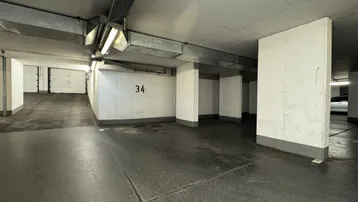 Geräumige Tiefgarage mit nummerierten Stellplätzen und sichtbaren Versorgungsleitungen an der Decke.