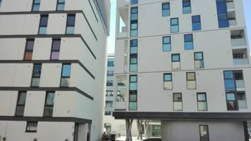Moderne Wohngebäude mit heller Fassade und vielen Fenstern in urbaner Umgebung.