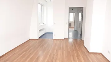 Helles, leeres Zimmer mit Laminatboden und weißen Wänden, bereit zur individuellen Gestaltung.