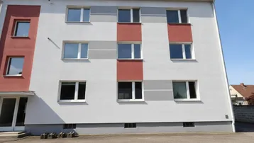 Modernisiertes Mehrfamilienhaus mit weißer Fassade, roten und grauen Farbakzenten.