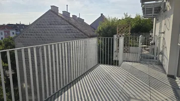 Geräumiger Balkon mit Fliesenboden und Blick auf die umliegenden Gebäude und den Himmel.