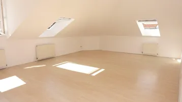 Heller Dachbodenraum mit schrägen Wänden, Dachfenstern und hellem Laminatboden, ideal für individuelle Gestaltung.