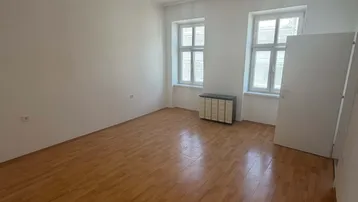 Helles Wohnzimmer mit Parkettboden, weißen Wänden und zwei Fenstern, bereit zur Einrichtung.