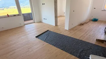 Heller Raum im Bau mit neuem Holzboden, Balkonzugang und Bergblick.