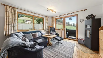 Gemütliches Wohnzimmer mit Ledersofa, Kaminofen und Zugang zu einem Balkon mit Bergblick.