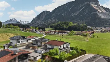 Panoramablick auf ein malerisches Dorf in einer grünen Berglandschaft mit vielen Häusern und Dächern.