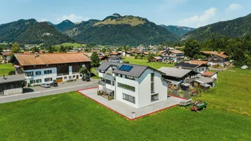 Luftaufnahme eines modernen Hauses mit Photovoltaikanlage und Bergblick in ländlicher Umgebung.