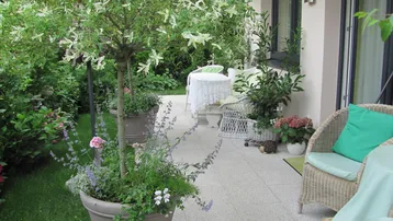 Gemütliche Terrasse mit Gartenmöbeln, vielen Pflanzen und Zugang zum grünen Gartenbereich.