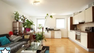 Helles, offenes Wohnzimmer mit integrierter Küche, Holzboden und vielen Pflanzen.