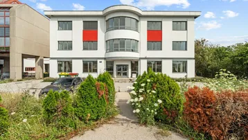 Modernes Bürogebäude mit weißer Fassade, roten Akzenten und gepflegter Grünanlage vor dem Eingang.