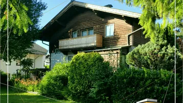 Traditionelles Holzhaus mit Balkon und gepflegtem Garten umgeben von Bäumen.