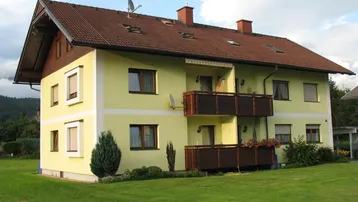 Mehrfamilienhaus mit gelber Fassade, braunem Dach und mehreren Balkonen in ländlicher Umgebung.