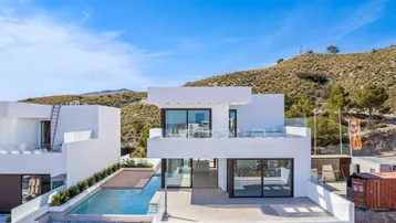 Moderne weiße Villa mit Infinity-Pool, großer Terrasse und Blick auf die umliegenden Hügel unter blauem Himmel.