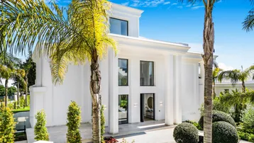 Elegante weiße Villa mit moderner Architektur und gepflegtem Vorgarten unter blauem Himmel.