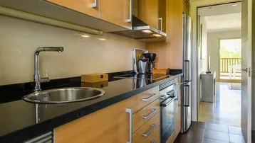 Funktionale Küche mit Holzschränken, schwarzer Arbeitsplatte und Blick in den Wohnbereich.