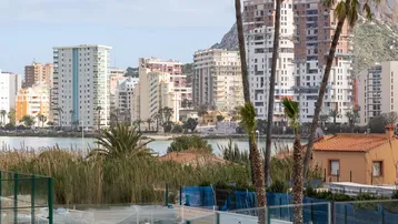 Gepflegter Außenbereich mit Pools, Tennisplatz, Palmen und Bergblick auf die Stadt.