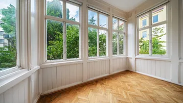 Heller Wintergarten mit großen Fenstern, Fischgrätparkett und einem schönen Blick ins Grüne.