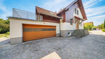 Einfamilienhaus mit integrierter Garage, gepflasterter Auffahrt und Balkon im Obergeschoss.
