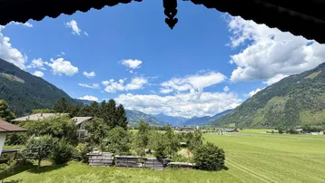 Weitläufiger Blick über grüne Wiesen und Berge unter blauem Himmel mit Wolken.