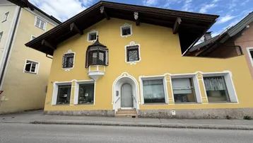Traditionelles gelbes Gebäude mit Erker und verzierten Dachdetails an einer Straße gelegen.